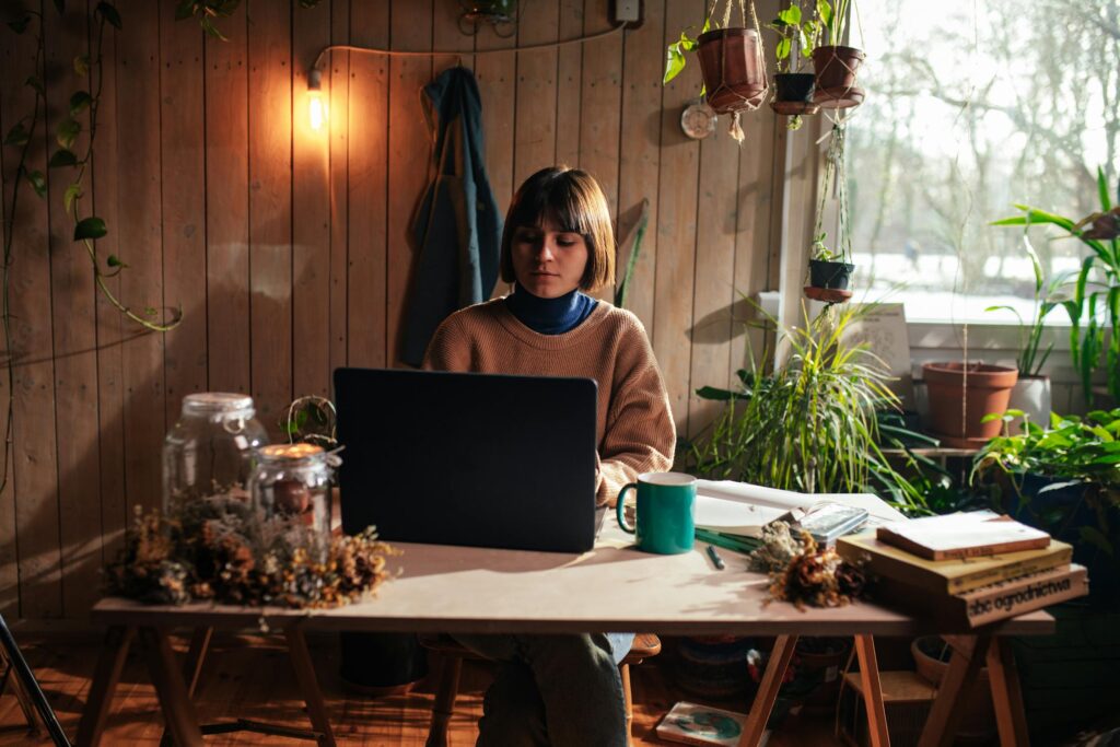 Woman working on a laptop surrounded by plants and books, developing digital products for monetization on their blog.